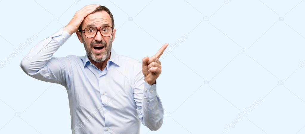 Middle age man with glasses pointing away side with finger isolated over blue background