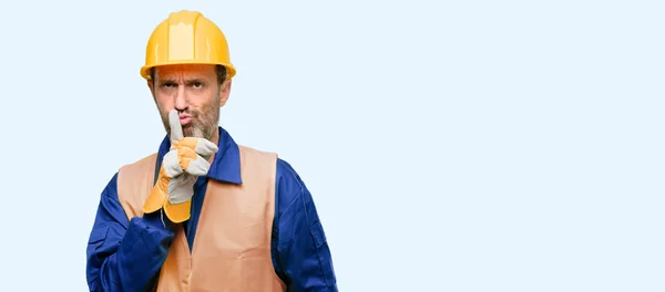 シニア エンジニア男 建設労働者 唇に人差し指を静かに求めます 沈黙と青い背景に分離された秘密の概念 — ストック写真