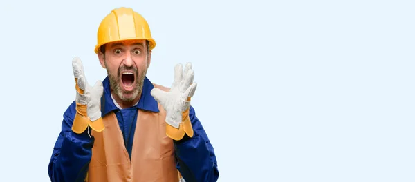 Senior engineer man, construction worker stressful keeping hands on head, terrified in panic, shouting isolated over blue background
