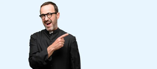 Priest religion man pointing away side with finger isolated over blue background