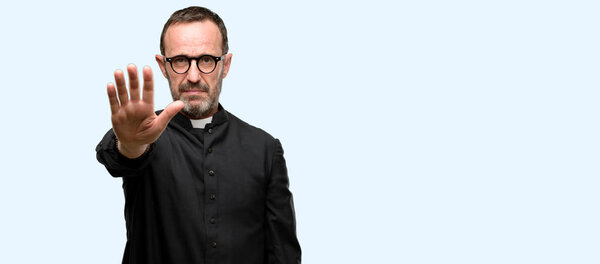 Priest religion man annoyed with bad attitude making stop sign with hand, saying no, expressing security, defense or restriction, maybe pushing isolated over blue background