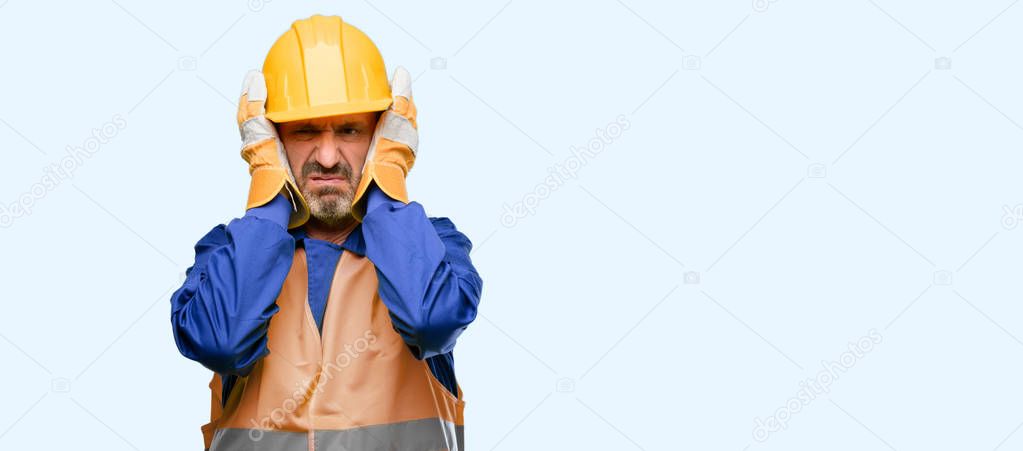 Senior engineer man, construction worker covering ears ignoring annoying loud noise, plugs ears to avoid hearing sound. Noisy music is a problem. isolated over blue background