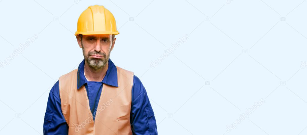 Senior engineer man, construction worker with sleepy expression, being overworked and tired isolated over blue background