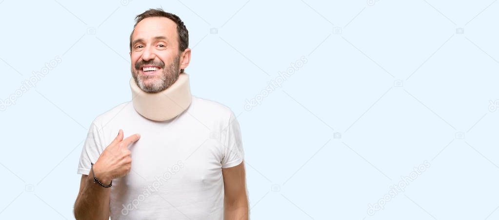 Injured senior man using a neck brace happy and surprised cheering expressing wow gesture, pointing with finger isolated over blue background
