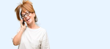 Aptal bir smartphone cep telefonu kullanarak konuşmak mutlu gözlüklü deli orta yaş kadın mavi arka plan izole