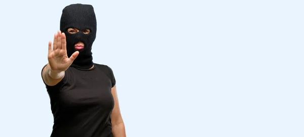 窃贼的恐怖妇女穿着巴拉克拉瓦滑雪面具恼怒与坏态度做停止标志用手 表示安全 防御或制约 可能推挤孤立的蓝色背景 — 图库照片
