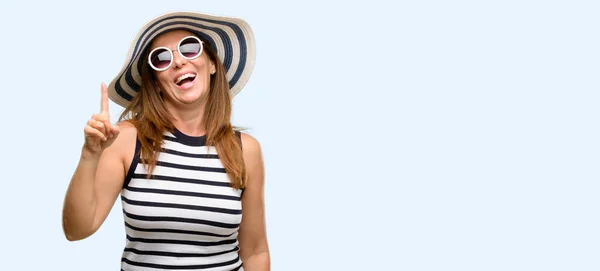 夏帽子と指でアウェイ側を指しているサングラスを身に着けている中年のクールな女性が青い背景を分離 — ストック写真