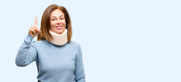 Injured woman wearing neck brace collar happy and surprised cheering expressing wow gesture pointing up isolated blue background
