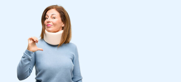 Injured woman wearing neck brace collar proud, excited and arrogant, pointing with victory face isolated blue background