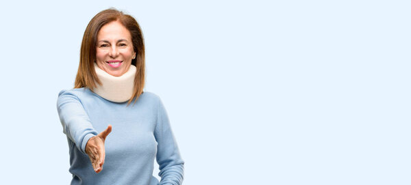 Injured woman wearing neck brace collar holds hands welcoming in handshake pose, expressing trust and success concept, greeting isolated blue background