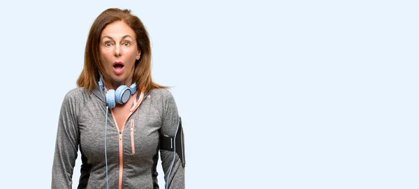 中年ジム トレーニング ヘッドフォン怖がってパニックを表現する衝撃の女性に合うし 分離の青い背景の恐怖 — ストック写真