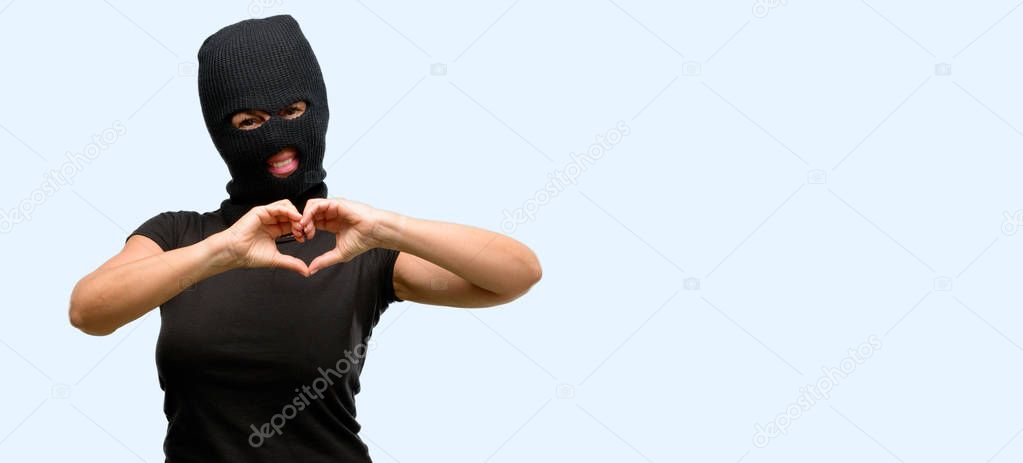 Burglar terrorist woman wearing balaclava ski mask happy showing love with hands in heart shape expressing healthy and marriage symbol isolated blue background
