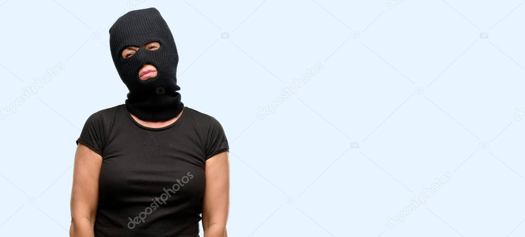 Burglar terrorist woman wearing balaclava ski mask with sleepy expression, being overworked and tired isolated blue background