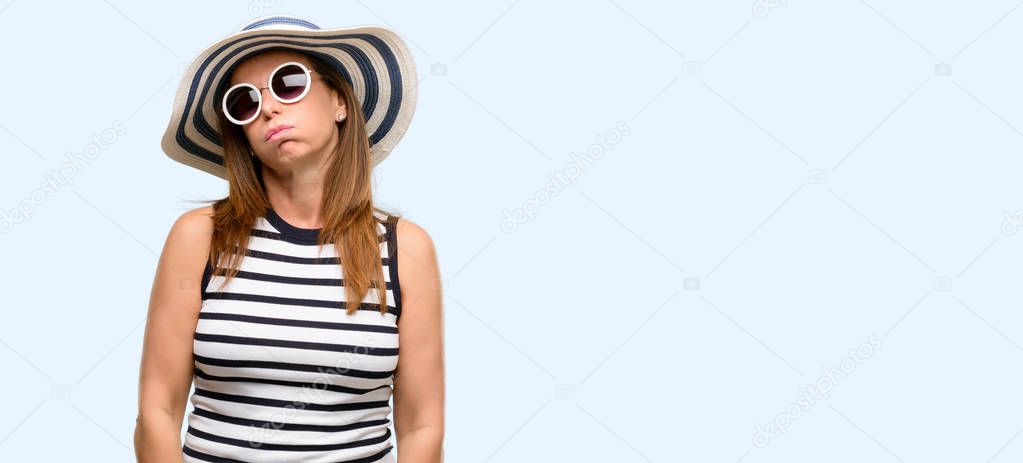 Middle age cool woman wearing summer hat and sunglasses with sleepy expression, being overworked and tired isolated blue background