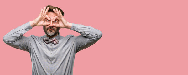 Мужчина средних лет, с бородой и галстуком-бабочкой, смотрящий в камеру пальцами в порядке жеста. Имитация бинокля
