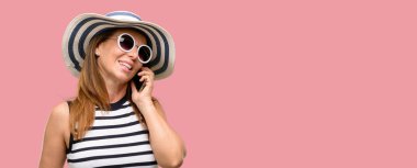 Orta yaş serin yaz şapka ve güneş gözlüğü smartphone cep telefonuyla konuşurken mutlu giyen kadın