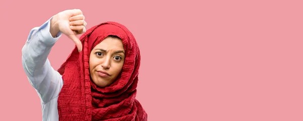 年轻的阿拉伯妇女戴着头巾显示拇指下来不愉快的迹象 不喜欢 否定的表达和反对 — 图库照片