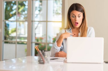 Parmak ile işaret öğrenci kadın masada dizüstü evde mutlu ve ifade wow jest, tezahürat ile