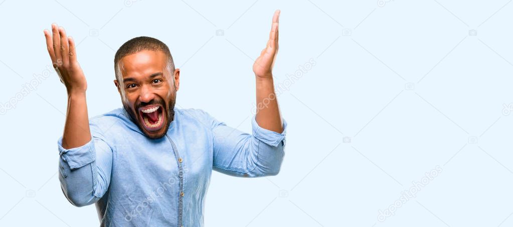 African american man with beard happy and surprised cheering expressing wow gesture isolated over blue background