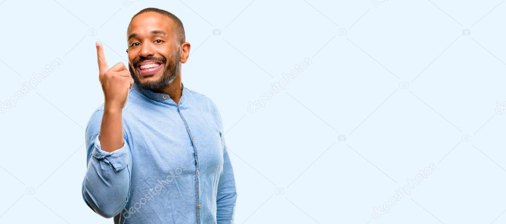 African american man with beard happy and surprised cheering expressing wow gesture pointing up isolated over blue background