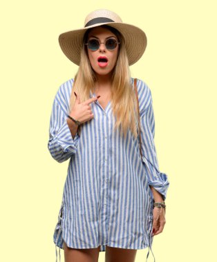 Parmak ile işaret güneş gözlüğü ve mutlu ve ifade wow jest, tezahürat yaz şapka giyen genç kadın