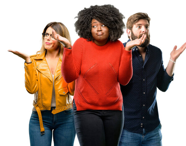 Group of three young men and women doubt expression, confuse and wonder concept, uncertain future shrugging shoulders