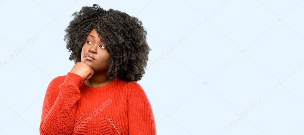 Beautiful african woman thinking and looking up expressing doubt and wonder, blue background