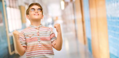 Yeşil gözleri mutlu ve heyecanlı kutluyor zafer büyük başarı, güç, enerji ve olumlu duygular ifade ile yakışıklı yürümeye başlayan çocuk. Yeni iş neşeli okul koridor az kutluyor