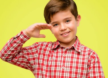 Bir şey boyutu kavram sarı arka plan üzerinde tutan yeşil gözlü yakışıklı yürümeye başlayan çocuk