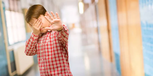 Handsome toddler child with green eyes stressful and shy keeping hand on head, tired and frustrated at school corridor