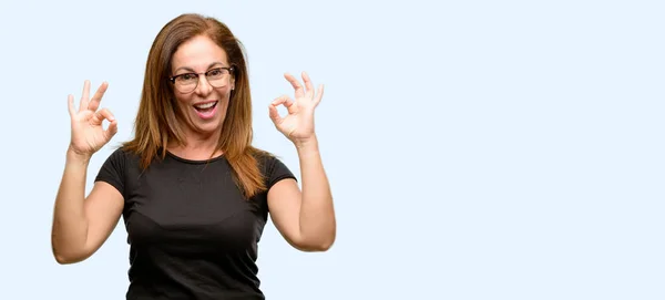 中年の女性が身に着けている黒いシャツと瞑想とリラクゼーションを表現する両方の手で の手話をやっているメガネ分離青色の背景 — ストック写真