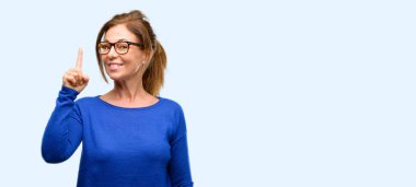 Yün kazak ve gözlük mutlu ve izole mavi arka plan işaret ifade wow jest tezahürat orta yaş kadın