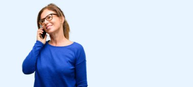 Yün kazak ve gözlük bir smartphone cep telefonu kullanarak konuşmak mutlu orta yaş kadın mavi arka plan izole