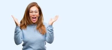 Yün kazak ve serin gözlük mutlu ve ifade wow izole jest mavi arka plan tezahürat orta yaş kadın