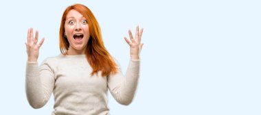 Güzel genç Kızıl saçlı kadın mutlu ve ifade wow jest tezahürat üzerinde mavi arka plan izole