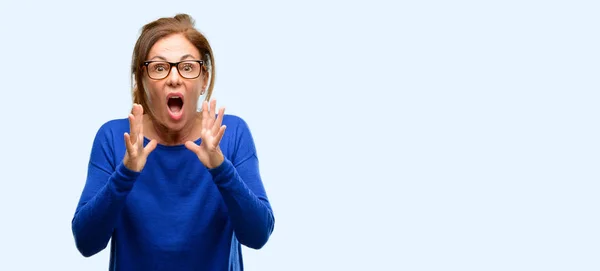 分離の青い背景を叫んで頭パニックで恐怖にウールのセーターとメガネ ストレス維持手を着て中年の女性 — ストック写真