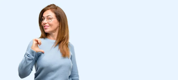 青色の背景に分離された中年女性の身に着けているウールのセーターと眼鏡クール誇りに思って 興奮して傲慢 ポイント勝利の顔 — ストック写真