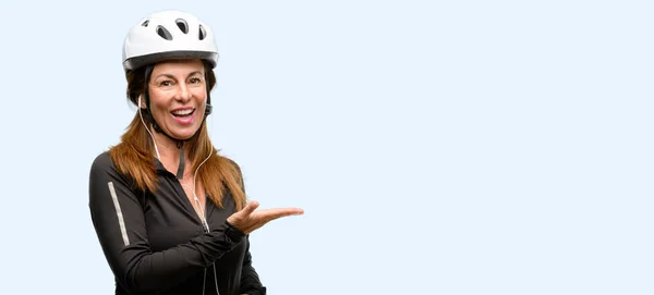 中年サイクリストの女性が空の手で何かを保持しているイヤホンを使用して分離された青色の背景 — ストック写真