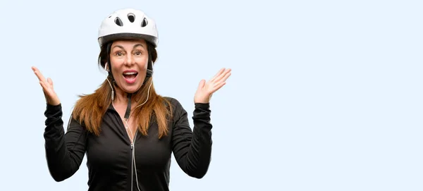 中年サイクリスト女性幸せと表現するすごいジェスチャー分離された青い背景を応援して驚いたのイヤホンを使用して — ストック写真