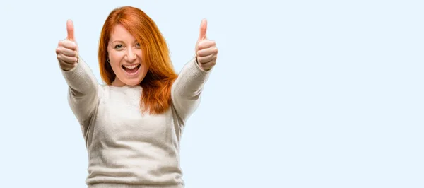 美丽的年轻红头发的女人站在高兴和积极与竖起大拇指同意一个大的微笑表达好手势孤立的蓝色背景 — 图库照片