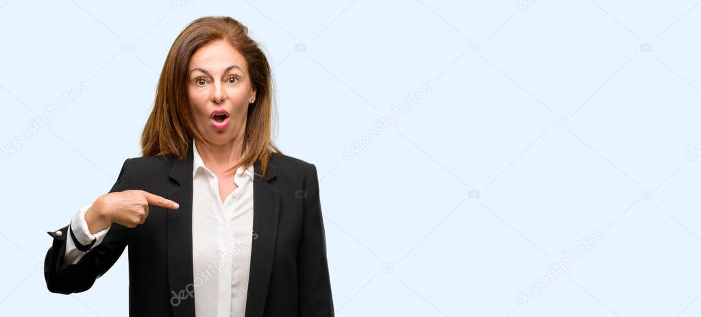Middle age woman wearing jacket happy and surprised cheering expressing wow gesture, pointing with finger isolated blue background