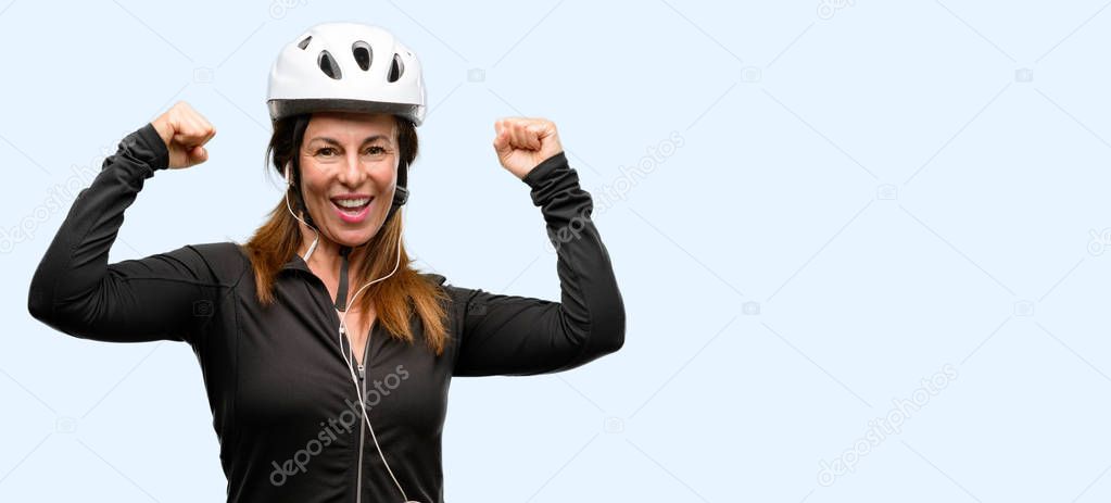 Middle age cyclist woman using earphones happy and excited celebrating victory expressing big success, power, energy and positive emotions. Celebrates new job joyful isolated blue background