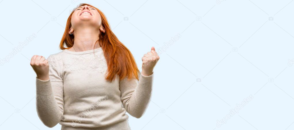 Beautiful young redhead woman happy and excited expressing winning gesture. Successful and celebrating victory, triumphant isolated over blue background