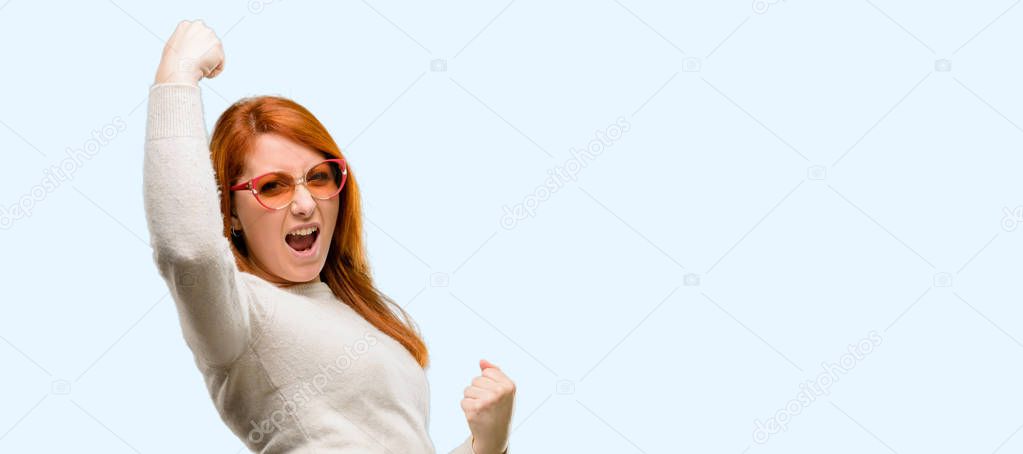 Beautiful young redhead woman happy and excited celebrating victory expressing big success, power, energy and positive emotions. Celebrates new job joyful isolated over blue background