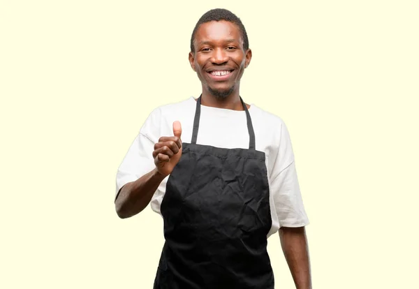 非洲男子店老板穿着围裙微笑着广泛显示竖起大拇指手势相机 表示喜欢和批准 — 图库照片