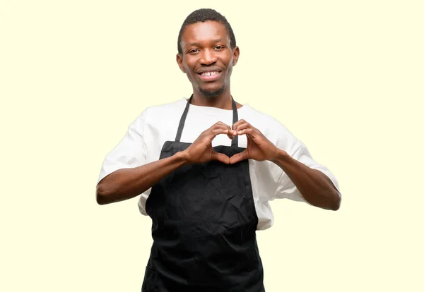 非洲男人店主穿着围裙高兴地显示爱与手在心脏形状表达健康和婚姻标志 — 图库照片