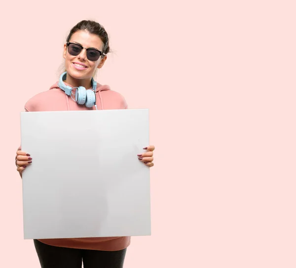 年轻运动妇女与耳机和太阳镜持有空白广告横幅 良好的广告海报 提供或公告 大纸广告牌 — 图库照片