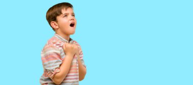 Yeşil gözleri mutlu ve heyecanlı kutluyor zafer büyük başarı, güç, enerji ve olumlu duygular ifade ile yakışıklı yürümeye başlayan çocuk. Mavi arka plan üzerinde yeni iş neşeli kutluyor