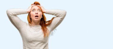 Güzel genç Kızıl saçlı kadın stresli tutmak ellerini kafasına, mavi arka plan üzerinde izole bağırarak panik içinde dehşete