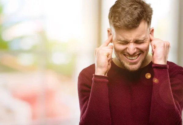 Handsome young man covering ears ignoring annoying loud noise, plugs ears to avoid hearing sound. Noisy music is a problem.